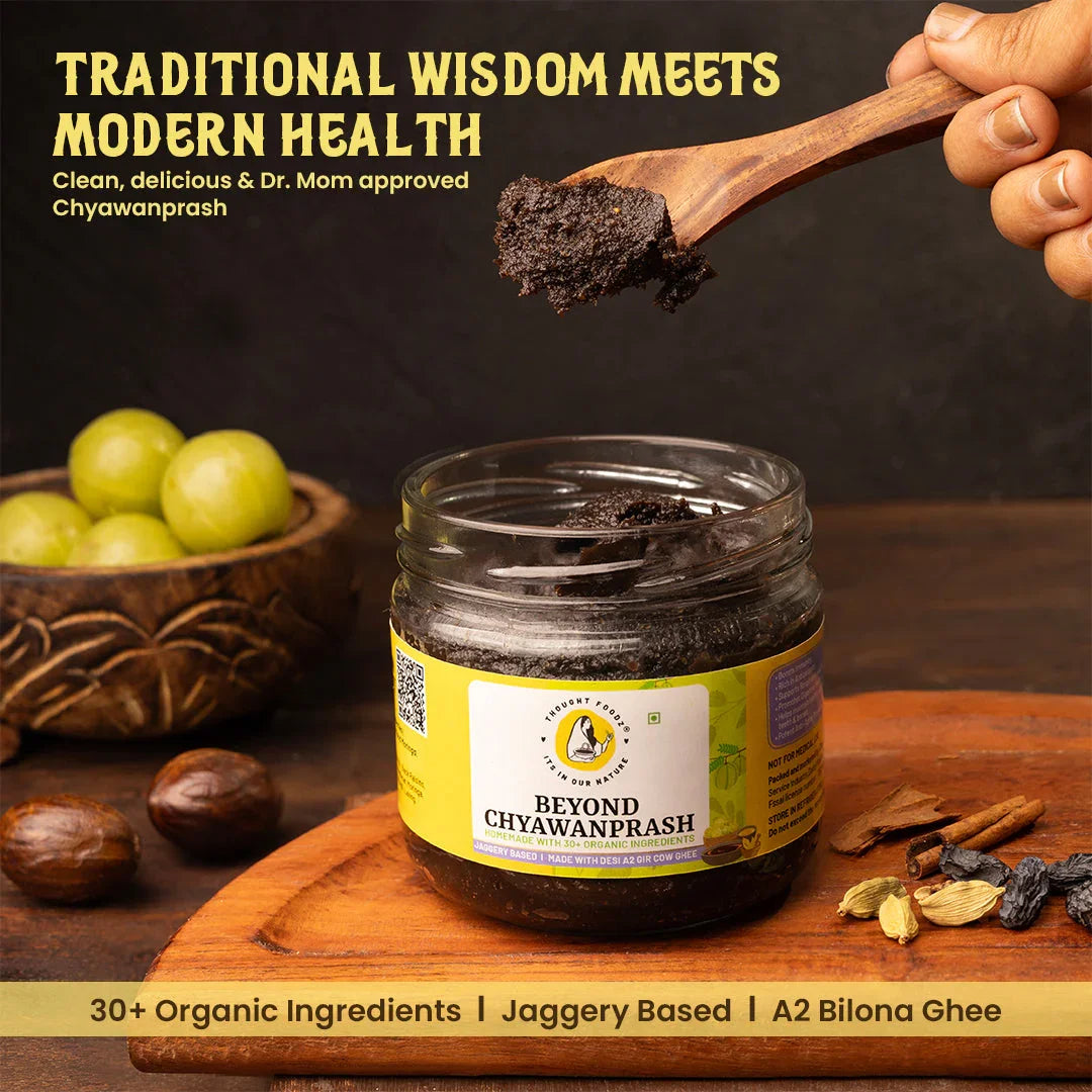 Jar of Beyond Chyawanprash by ThoughtFoodz with wooden spoon, herbs, and amla fruit on table