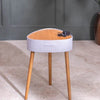 Small round stool with wooden legs and a light gray cushioned seat against a neutral background.