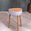 Small round stool with wooden legs and a light gray upholstered seat against a dark gray wall.