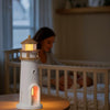 Lighthouse-shaped soft night light on a table with a blurred background of a person in a crib.