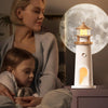 Woman and child sitting together with a lighthouse-shaped lamp in the foreground and a moonlit sky in the background.